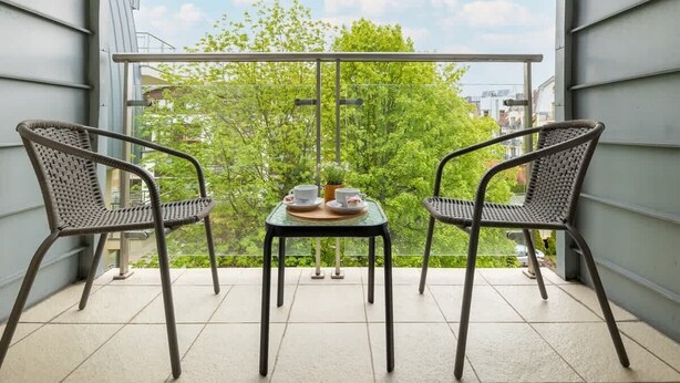 Ein Balkon mit zwei Korbstühlen und einem kleinen Tisch mit Tassen und Untertassen.
