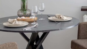 Ein runder Esstisch mit Blumen in einer Vase, zwei Weingläsern und sorgfältig gedeckten Tellern und Besteck.