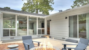 A modern outdoor patio with a fire pit, seating, and large glass doors leading to an interior space.