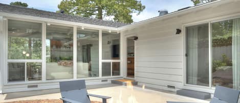 A modern outdoor patio with a fire pit, seating, and large glass doors leading to an interior space.