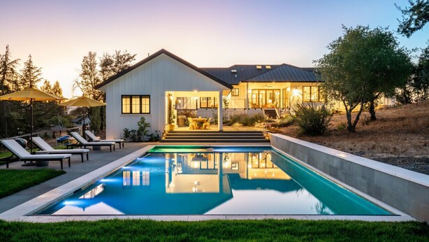 Une maison moderne dotée d’une piscine, d’un espace salon extérieur et d’une entrée bien éclairée.