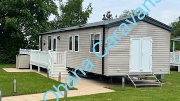 A mobile home with a porch, a small deck, and a ramp for accessibility.