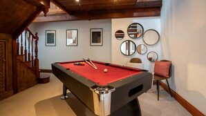 Une table de billard dans une pièce avec un escalier en bois, des tableaux encadrés au mur et une moquette rouge.