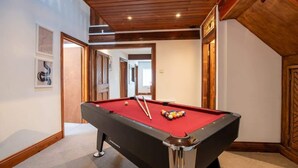 Une table de billard dans une pièce dont le plafond est orné de poutres en bois et dont les murs sont décorés d’œuvres d’art encadrées.