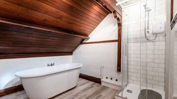 A bathroom with a freestanding bathtub, a glass-enclosed shower, and wooden ceiling beams.