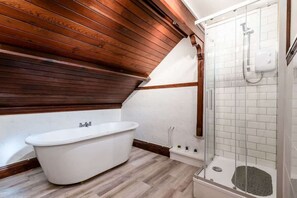 Un baño con una bañera independiente, una ducha con cerramiento de vidrio y vigas de madera en el techo.