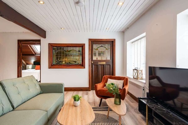 A living room with a green sofa, an orange armchair, a wooden coffee table, and a TV.