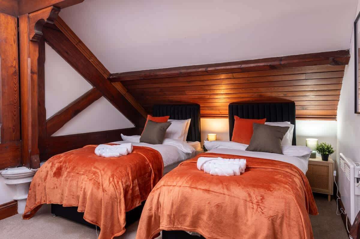 A bedroom with two beds, wooden beams, and a sloped ceiling.