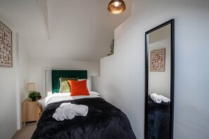 A modern hotel room with a large bed, a nightstand with a lamp, a mirror, and decorative wall art.