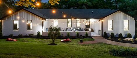 Una casa de dos pisos con un porche cubierto, ventanas amplias y luces colgantes.