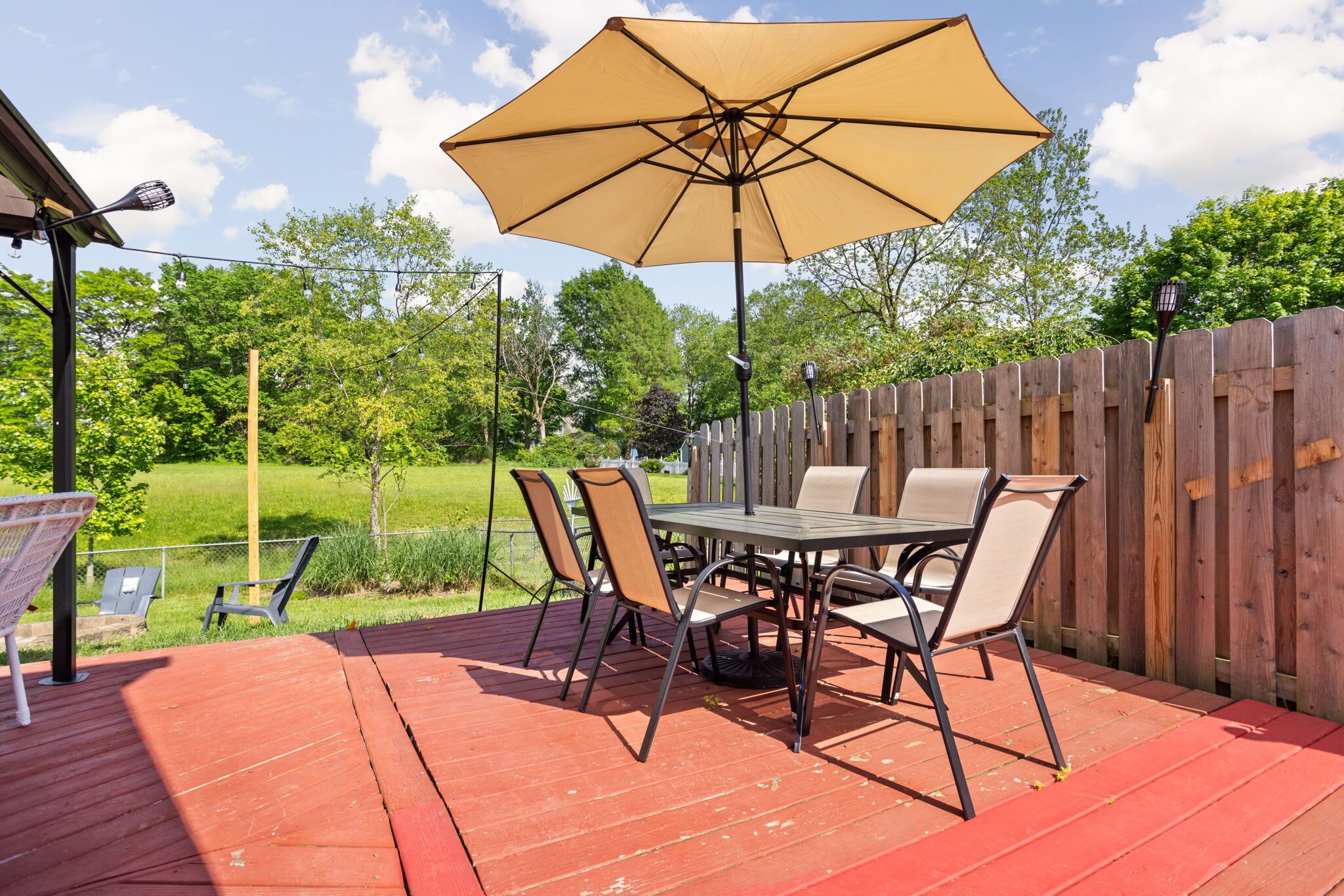 Une terrasse avec une table et des chaises, un grand parasol et une clôture en bois.