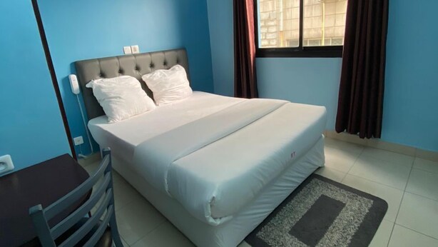 A bedroom with a bed, a chair, a table, an air conditioner, and a window with curtains. - TOMEDI HOTEL  (Douala)