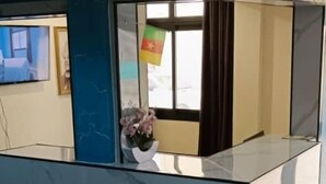 A reception area with a marble counter, a flag, and a window with curtains. - TOMEDI HOTEL  (Douala)
