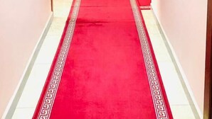 A hallway with a red carpet, doors on both sides, and a light-colored wall. - TOMEDI HOTEL  (Douala)