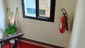 A staircase with a red carpet, a window with a black frame, and a fire extinguisher mounted on the wall. - TOMEDI HOTEL  (Douala)