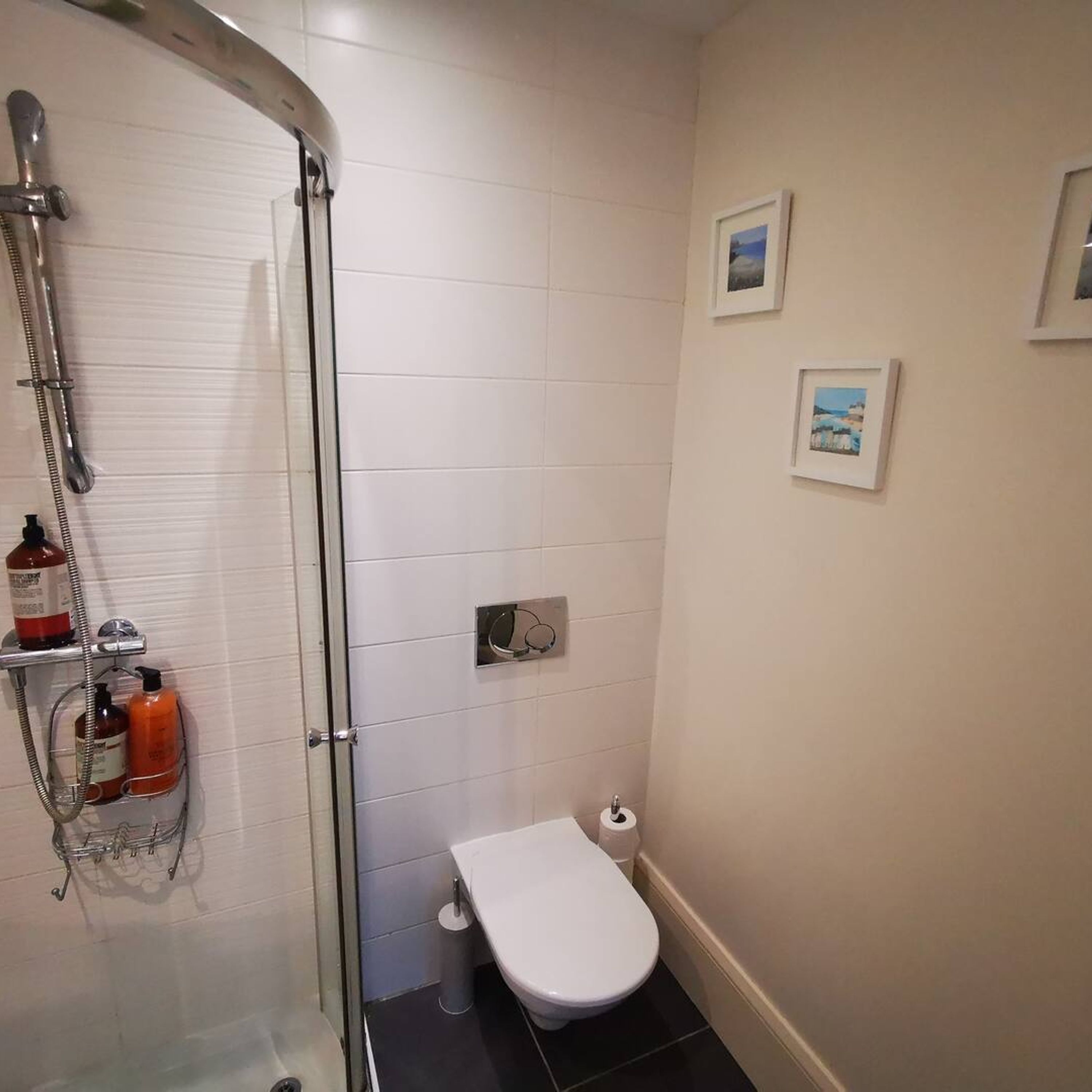 Une petite salle de bain avec une douche à parois de verre, des toilettes blanches et une petite poubelle.