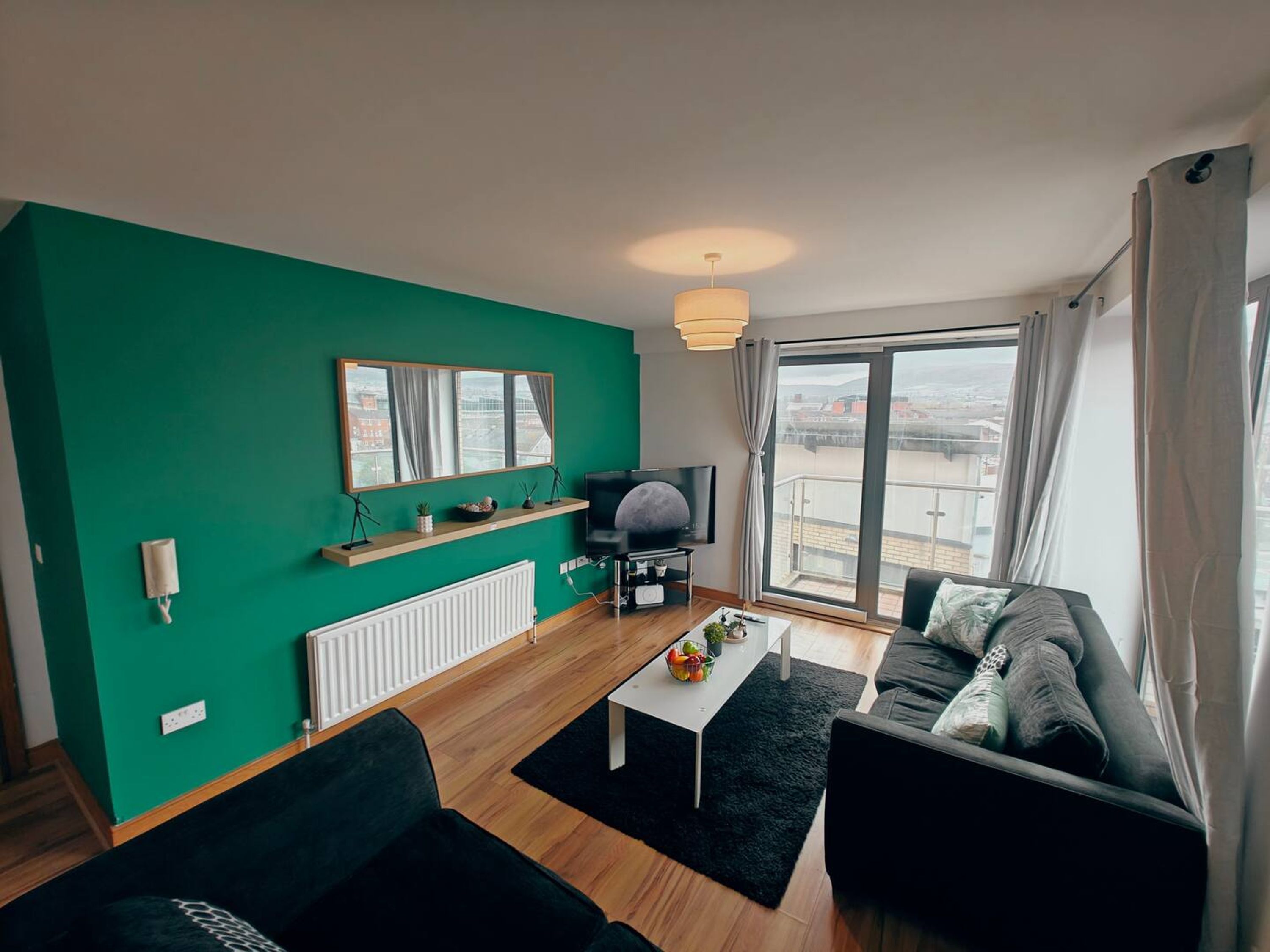 A modern living room with a green wall, a large window, a flat-screen TV, a sofa, and a coffee table.