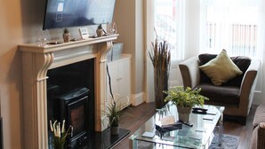A living room with a flat-screen TV on a mantel, a fireplace, a sofa, and a coffee table. - 4 Bed Boutique House Lisburn Road (Belfast)