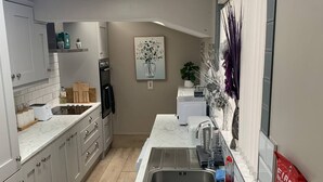 A modern kitchen with white cabinets, a marble countertop, a stainless steel sink, and a painting of a tree. - 4 Bed Boutique House Lisburn Road (Belfast)