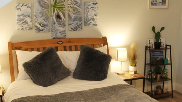 A neatly made bed with a grey quilt, two dark grey pillows, and two folded white towels. - 4 Bed Boutique House Lisburn Road (Belfast)