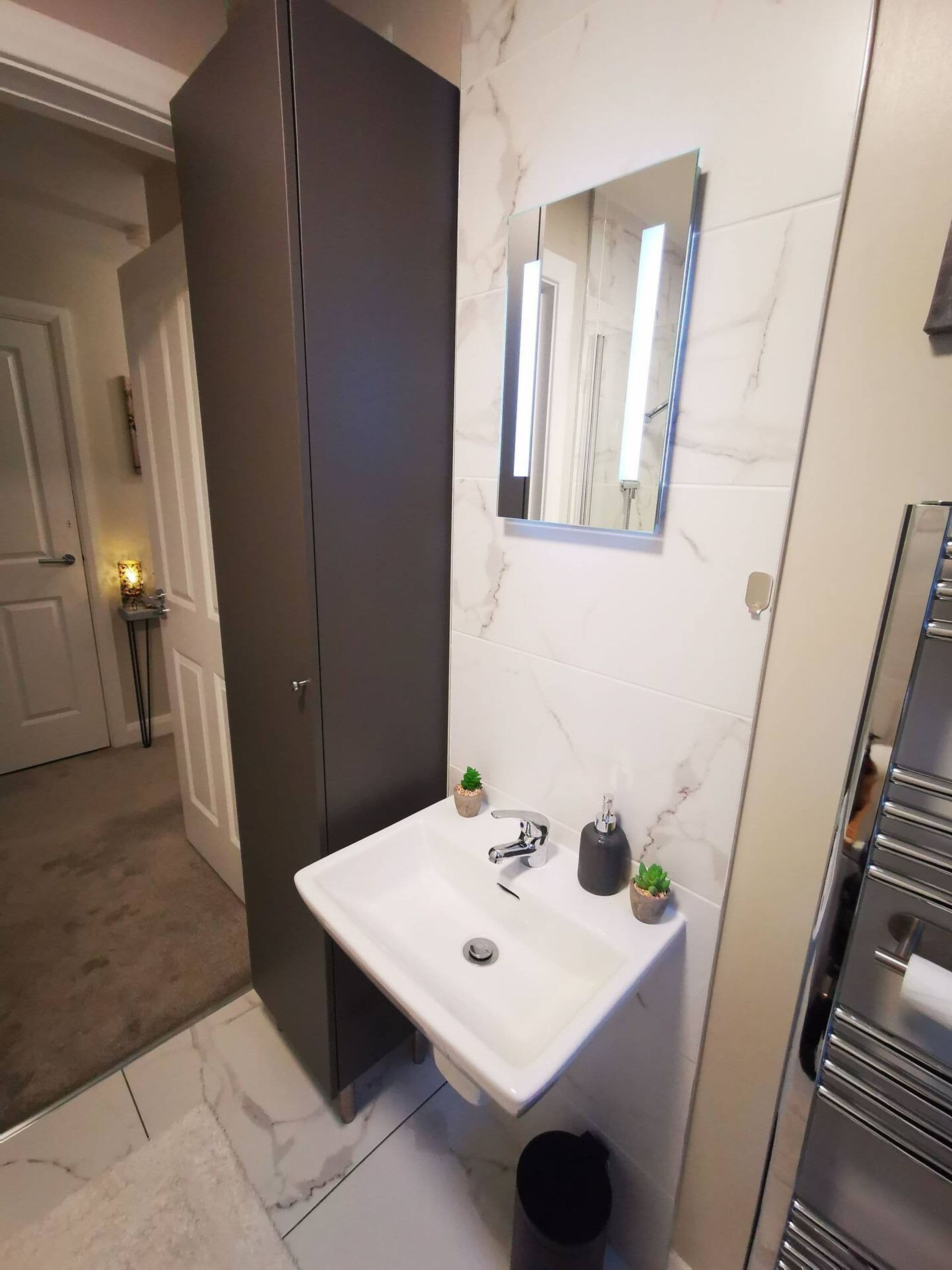 A modern bathroom with a marble-tiled wall, a white sink, a mirror, and a small potted plant.
