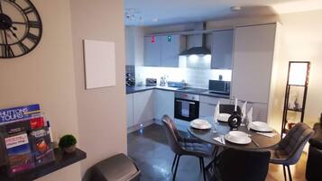A modern kitchen with a dining area, a trash bin, and a clock on the wall.