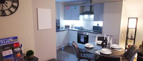 A modern kitchen with a dining area, a trash bin, and a clock on the wall.