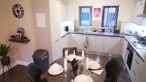 Una cocina compacta con zona de comedor, un reloj en la pared y un pequeño cubo de basura.