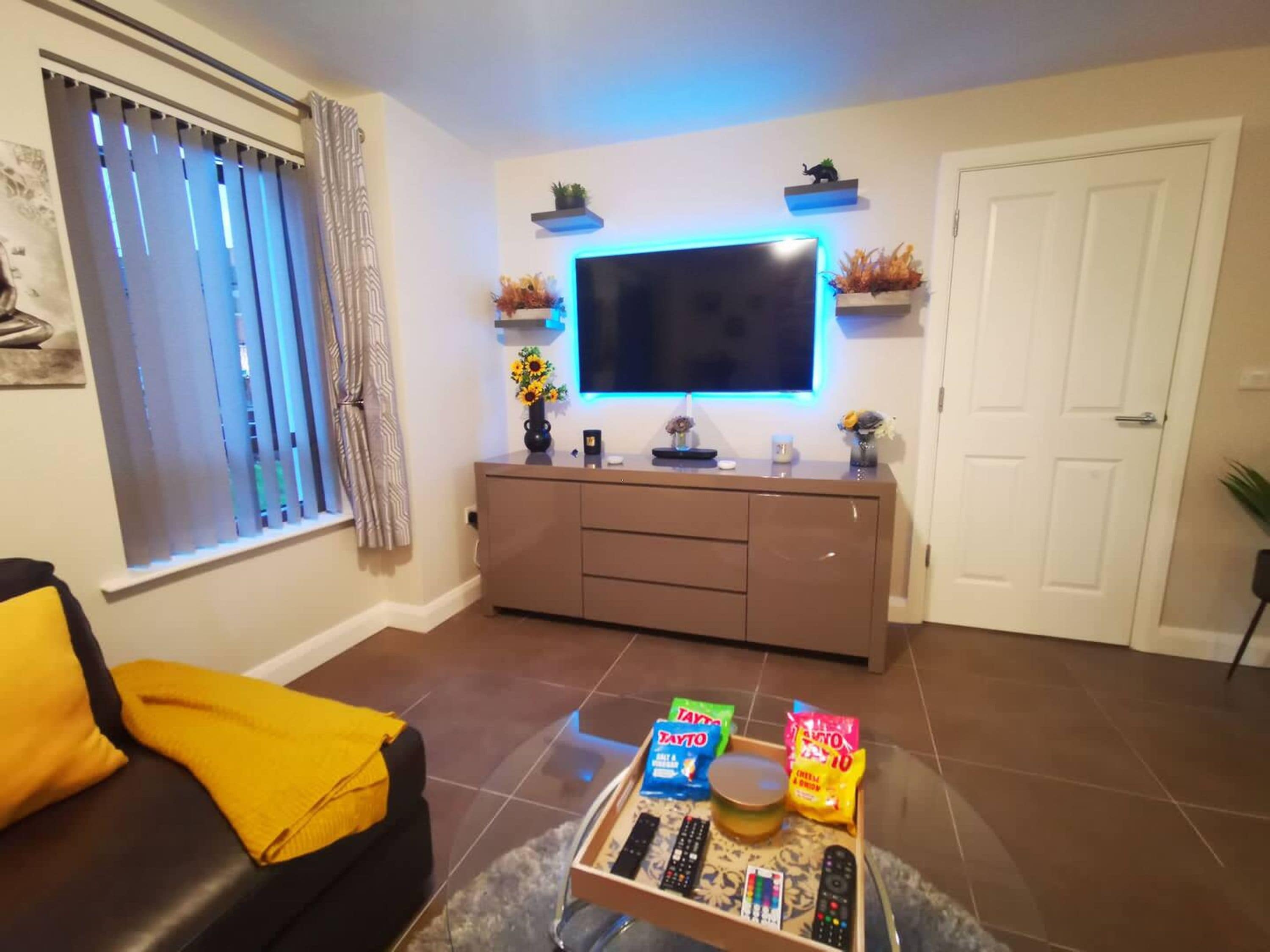Un salon équipé d’un téléviseur à écran plat, d’un canapé, d’une table basse avec des collations et des télécommandes, et d’une porte.