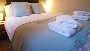 Una cama bien hecha con sábanas y almohadas blancas, un cuadro de un león en la pared y una pila de toallas dobladas sobre la cama.