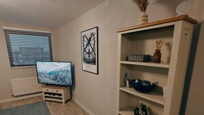 Ein Wohnzimmer mit Fernseher, Bücherregal und gerahmten Bildern an der Wand.