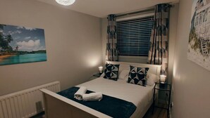 Ein Schlafzimmer mit Bett, einem Fenster mit Vorhängen, einem Bild an der Wand und einer Lampe.