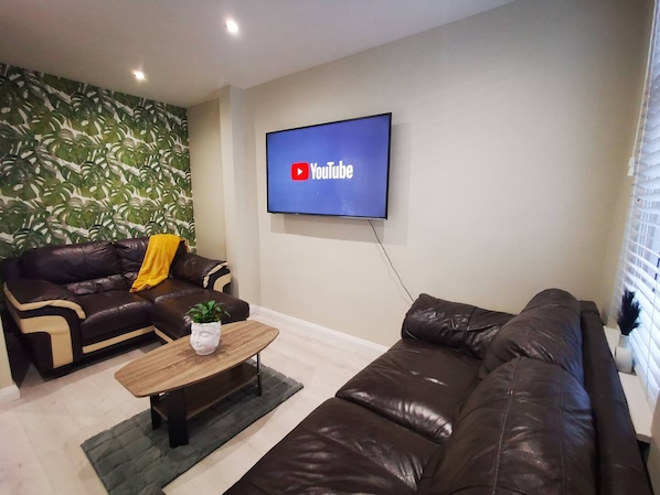 Una sala de estar con un sofá de cuero marrón, una mesa de centro de madera y un televisor en la pared mostrando el logotipo de YouTube.