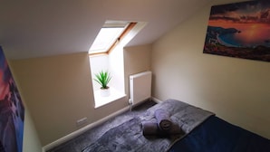 Ein kleines Schlafzimmer mit Dachfenster, Heizkörper, zusammengerolltem Handtuch und einem Bild an der Wand.