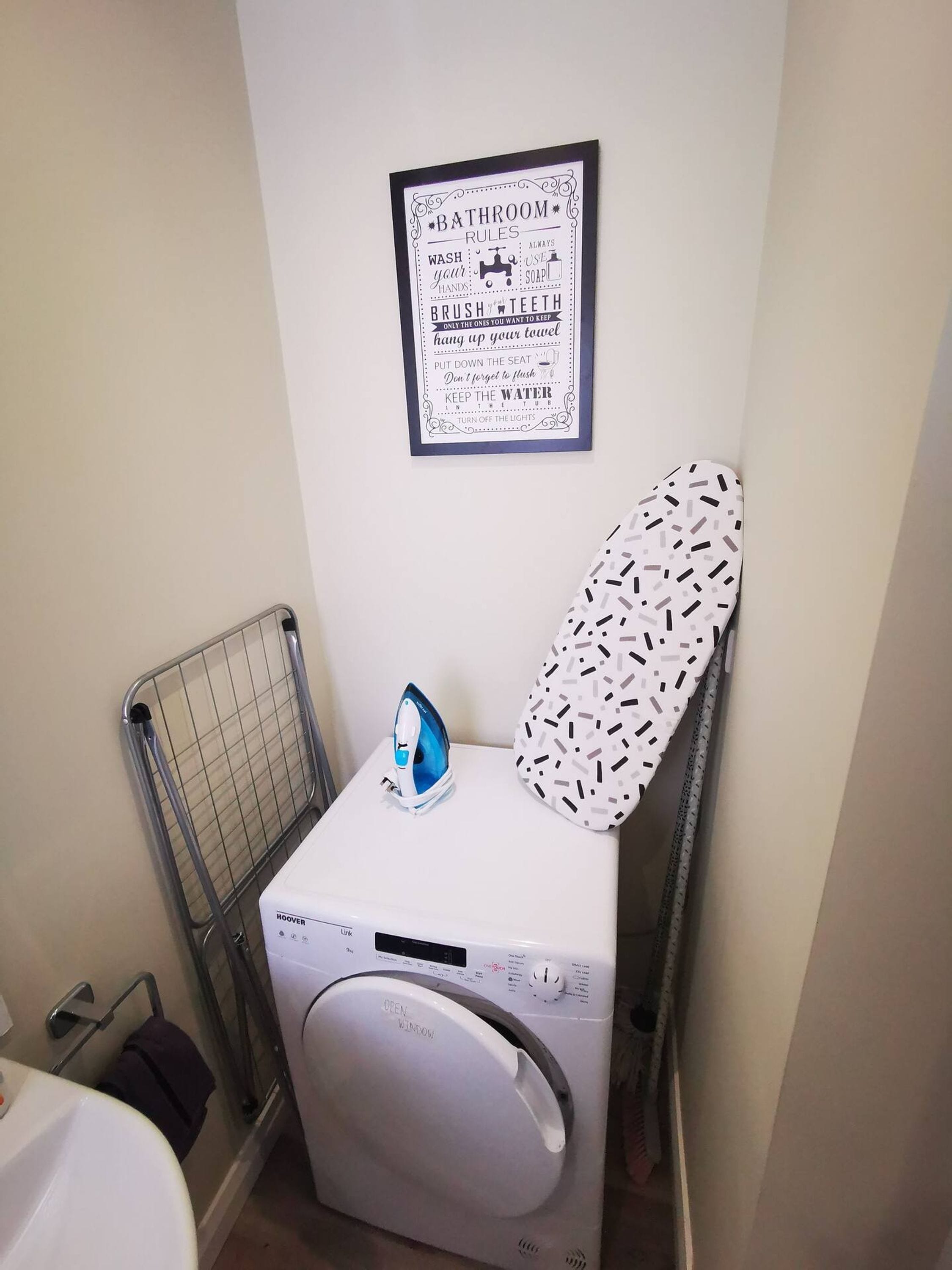 A laundry area with a washing machine, an iron, and a wall-mounted sign with bathroom rules.