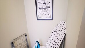 Un espace buanderie équipé d’un lave-linge, d’un fer à repasser et d’un panneau affiché au mur indiquant les règles à respecter dans la salle de bain.