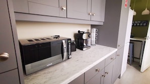 Eine Küche mit grauen Schränken, einer Mikrowelle, einer Kaffeemaschine und einer Kaffeetasse auf der Arbeitsfläche.