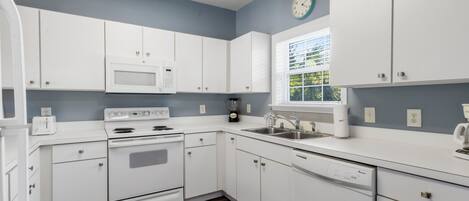 A modern kitchen with white cabinets, a microwave, stove, and dishwasher.
