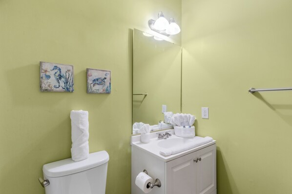 A bathroom with a toilet, a sink with a mirror, and two wall-mounted artwork pieces.