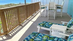 Un balcón con barandilla de madera, sillones de descanso blancos con cojines de estampado tropical azul y una mesa con sillas.