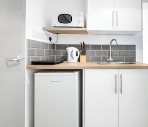 A compact kitchen with a microwave, kettle, sink, and a dishwasher.
