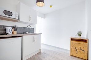 A modern kitchen with white cabinets, a microwave, a coffee maker, and a small refrigerator.