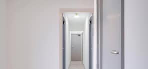 Un pasillo estrecho con una puerta al final, una lámpara arriba y un picaporte a la derecha.