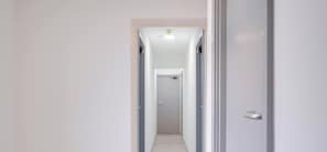 Un pasillo estrecho con una puerta al final, una lámpara arriba y un picaporte a la derecha.