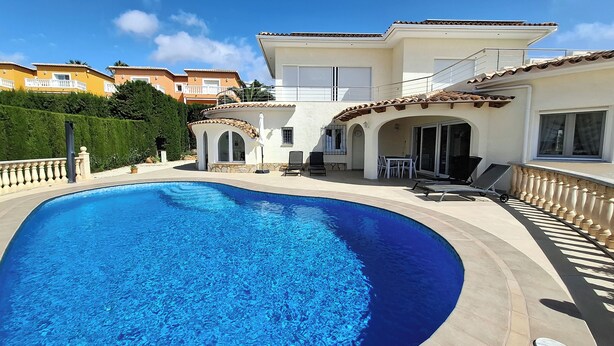 A swimming pool with a curved edge, a patio area with chairs and a table, and a building with a balcony. - Luxury Villa with Peñon view. 5 Minutes to the beach (Calpe)