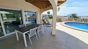 Um pátio externo com mesa e cadeiras, piscina e vista da região.