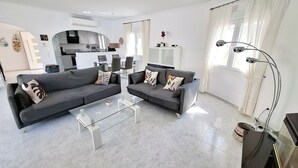 A modern living room with two grey sofas, a glass coffee table, and a kitchen in the background. - Luxury Villa with Peñon view. 5 Minutes to the beach (Calpe)