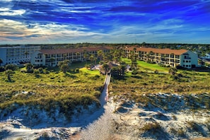 A resort with multiple-story buildings, a central courtyard with palm trees, and a sandy beach area.