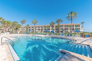 A hotel with a swimming pool, palm trees, and blue umbrellas. - Cozy Two Level Condo Overlooking the Ocean and Beachside Pool! (St. Augustine)