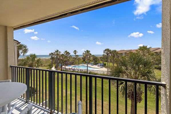 A balcony with a view of a pool and palm trees. - Cozy Two Level Condo Overlooking the Ocean and Beachside Pool! (St. Augustine)